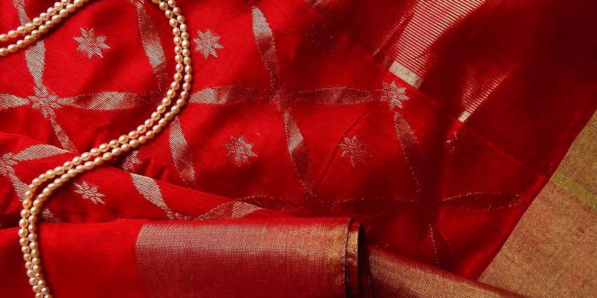 A mesmerising view of a golden and white pearl necklace kept on a red and gold saree.