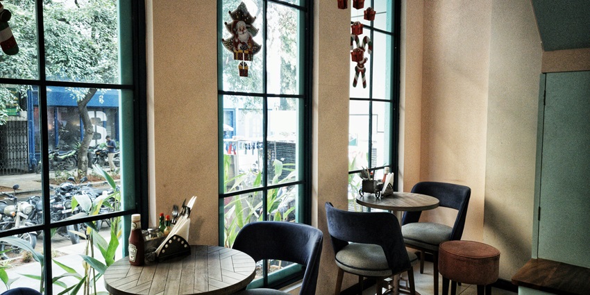 View of two brown wooden tables and grey chairs in a cafe with three big windows.