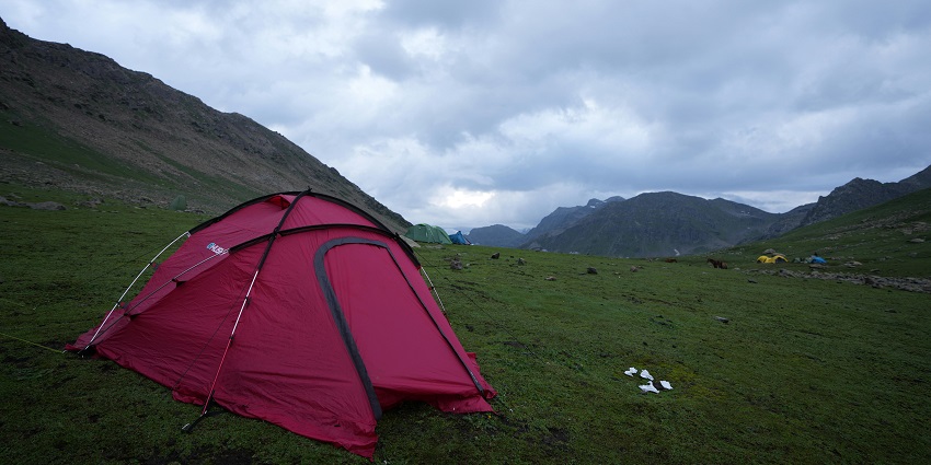 Image of red tent around lush green mountains and under clear blue sky.
