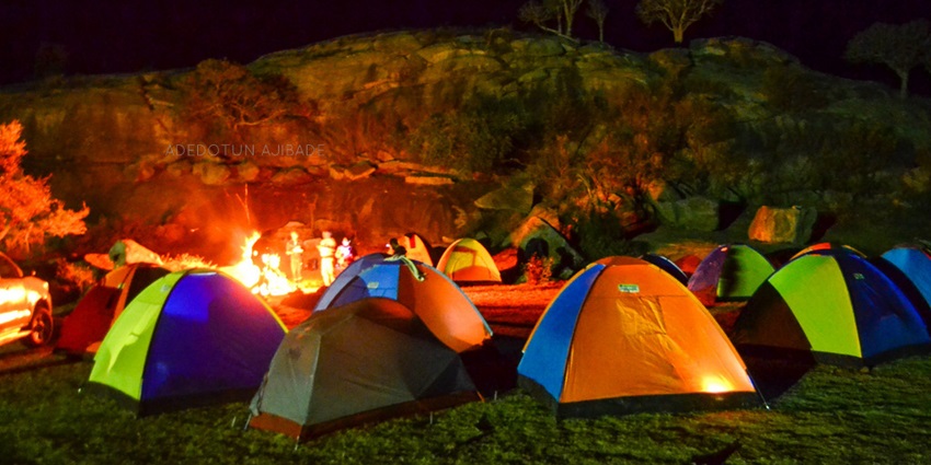 Numerous tents placed in a forest with a bonfire at night