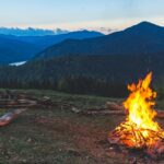 A stunning view of a bonfire in an open lush green grass field during the evening.