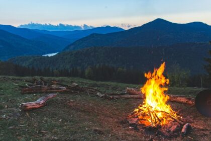 A stunning view of a bonfire in an open lush green grass field during the evening.