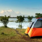 Camping tent in orange colour near lakeside - one of the best sites for camping in Shillong