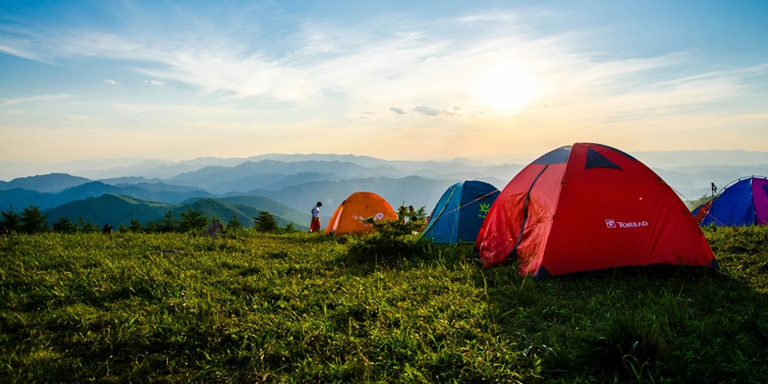 Dome tents pitched on a grassy hilltop, overlooking expansive mountain ranges and valleys.