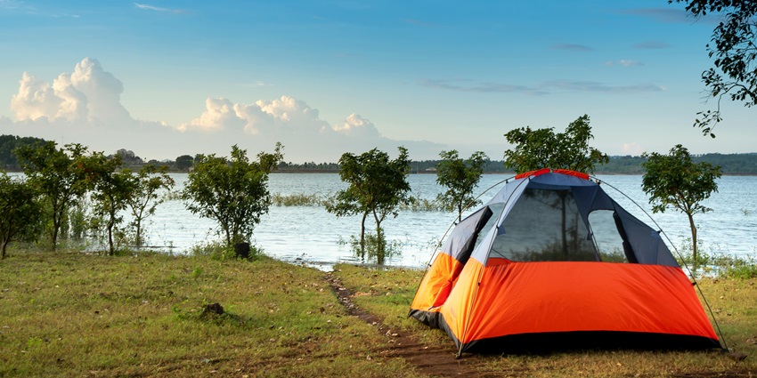 Dome tent set up near a calm body of water, surrounded by trees and natural scenery.