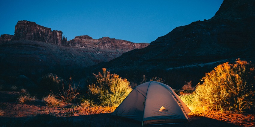 Camping tent beside a mountain at night, under a starry sky with a peaceful, serene setting.