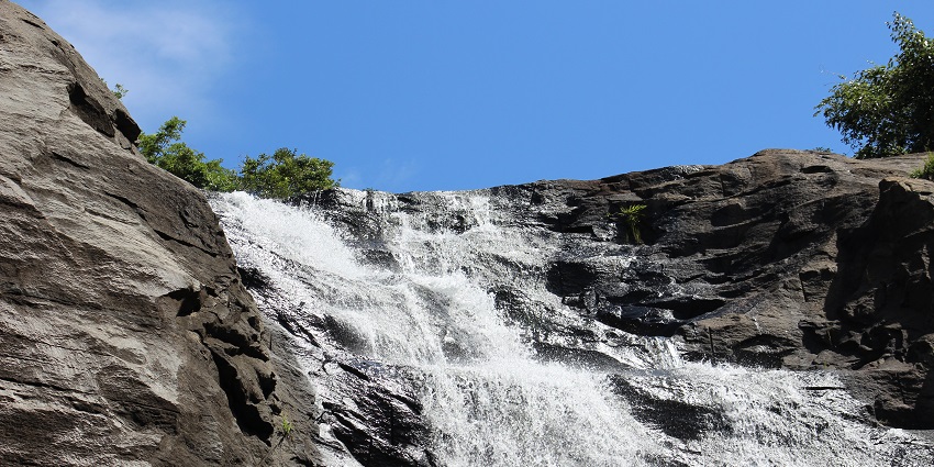 A beautiful waterfall around a hilly area with greenery and tall trees