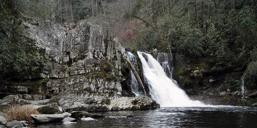 A beautiful waterfall around a hilly area with greenery and tall trees