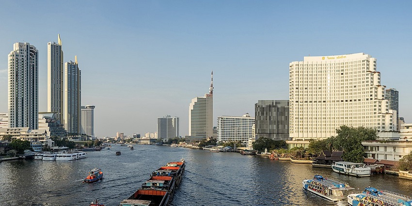 Chao Phraya River with boats and Bangkok's skyline in the background during sunset.
