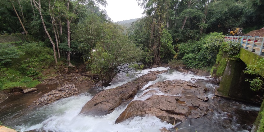 A picture of a cascading waterfall at a rocky hill, with trees and greenery all around