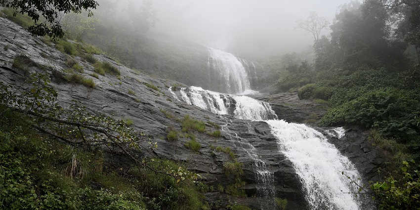 A picture of a majestic waterfall with water cascading down a rocky hill, surrounded by greenery