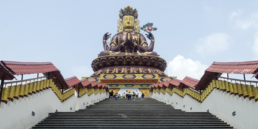 A picture of a staircase leading to a majestic and colourful statue of a Buddhist deity