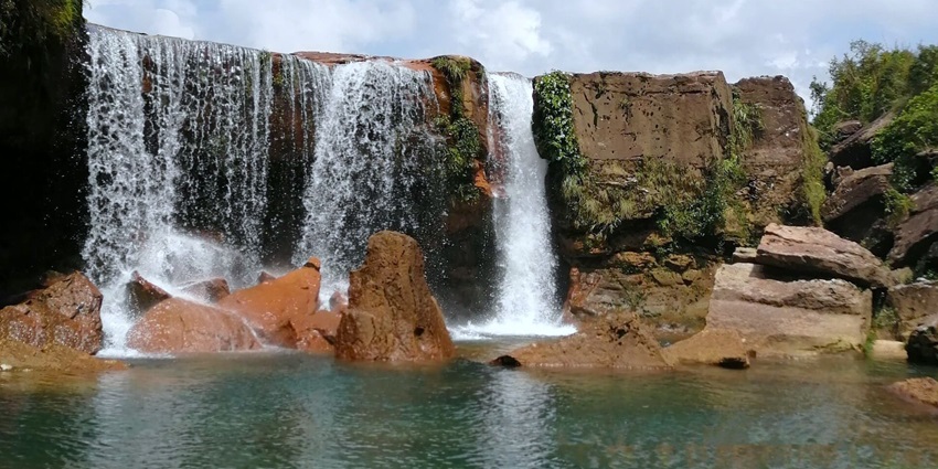 A beautiful waterfall surrounded by rocks and greenery with a pond in front
