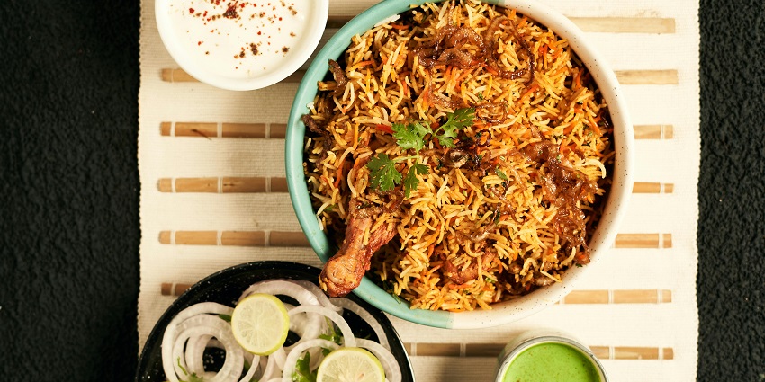 Vibrant bowl of chicken biryani topped with herbs and served with a side of raita.