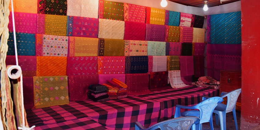 A view of sarees on a display with chairs in front of an open shop during the daytime.