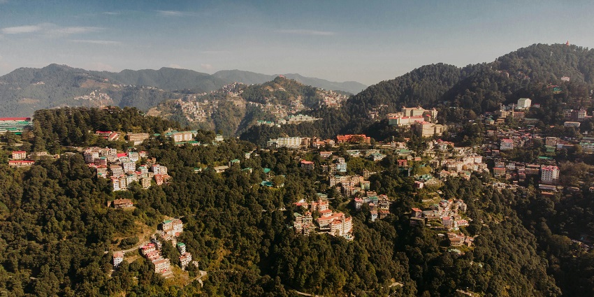 Aerial view of a city in the Himalayas covered in the dense lush forest in summers