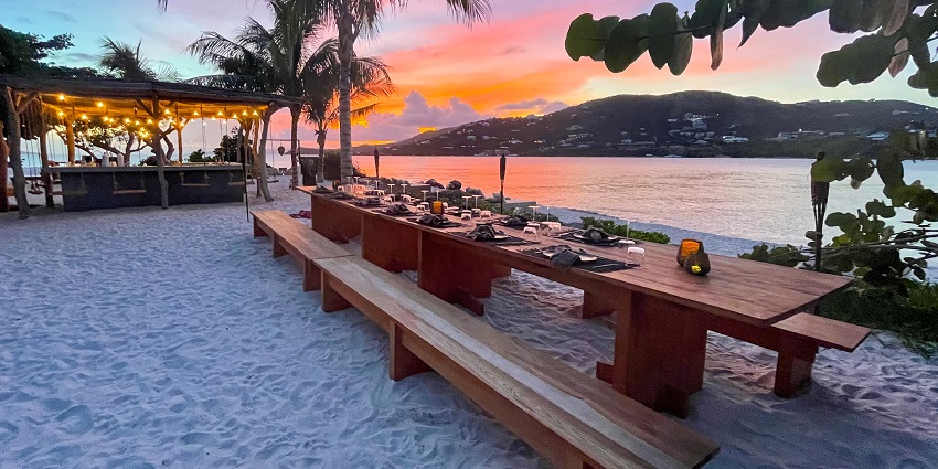 Beachside dining setup at The Aerial BVI with tables on a sandy shore.