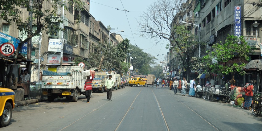 A picture of a street in Kolkata with tram tracks on the road and shops on both sides