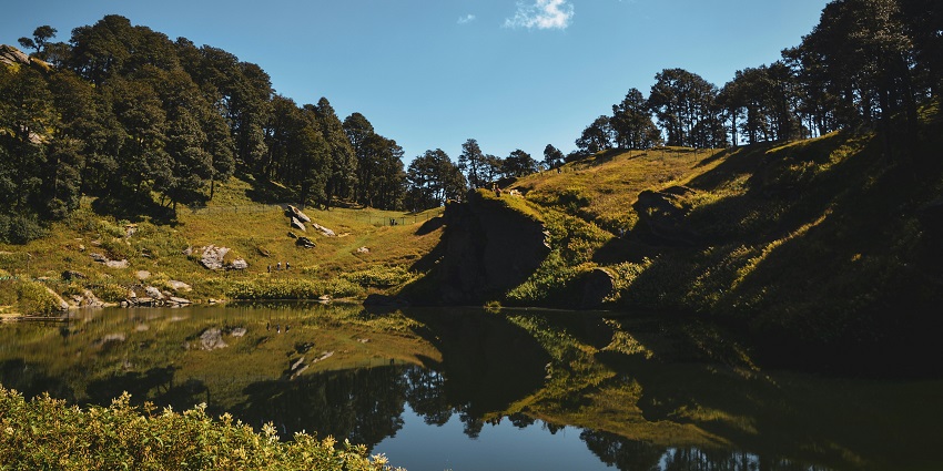 A stunning view of a water body in a lush green forest with mountains in the backdrop.