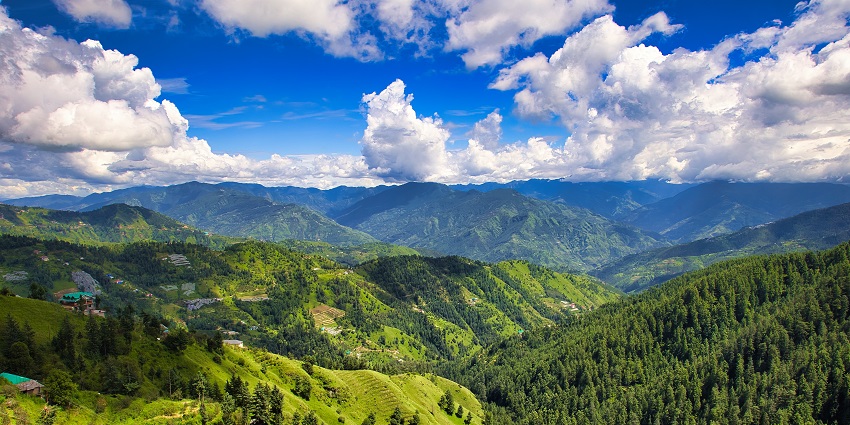 A vibrant mountain landscape under a clear blue sky, showcasing rolling hills and greenery.