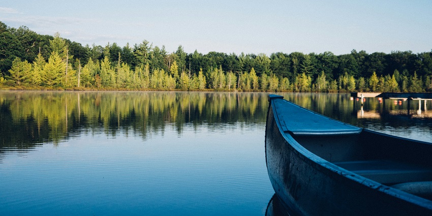 A serene view of shimmering waters, lush greenery, and a boat resting on the Damdama Lake.