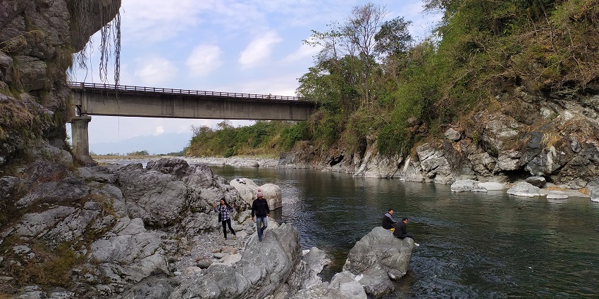 A picture of a picnic spot where people are enjoying by the river surrounded by hills