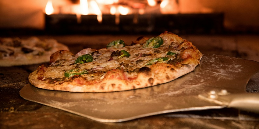 A picture showing the making of a pizza in a clay oven at a restaurant