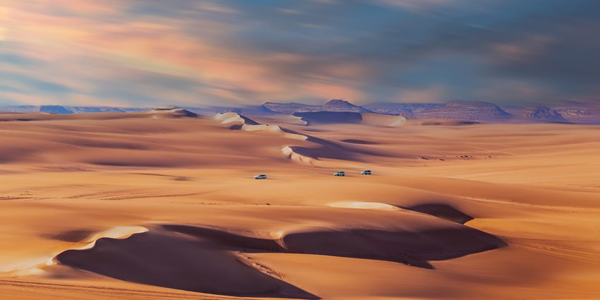 A picture of a large desert with vehicles moving at a faraway distance, enjoying a desert safari.