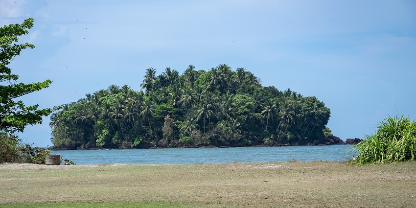 A picture taken from a beach with a waterbody in front and a big island in the background