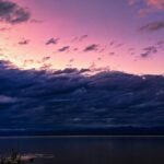 A breathtaking view of a purple-coloured sky with a body of water under dense clouds.