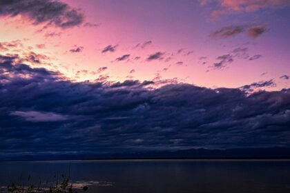 A breathtaking view of a purple-coloured sky with a body of water under dense clouds.