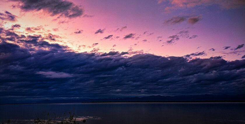 A breathtaking view of a purple-coloured sky with a body of water under dense clouds.