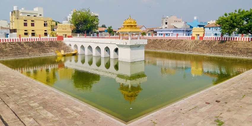 A picture of a holy pond in the middle of a temple complex with stairs on all sides