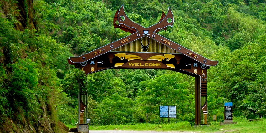 A picture of a road on mountains with a signboard welcoming commuters