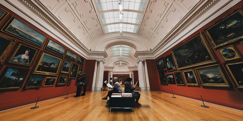 A mesmerising view of different paintings in an art gallery with three people in it.