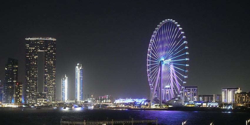 A picture of a giant wheel nearby the tall buildings of Dubai during nighttime