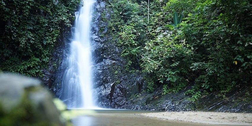 Durian Perangin Waterfall in Langkawi, Malaysia, cascading over moss-covered rocks amidst forest.
