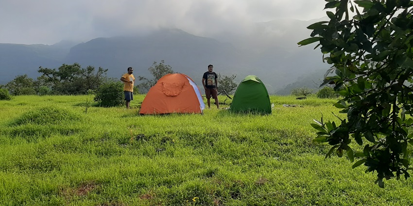 A picture of camping tents on top of a lush green hill with people enjoying the views