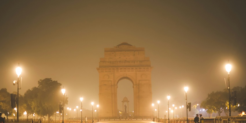 A nighttime view of the iconic India Gate dazzling with lights and covered with mist.