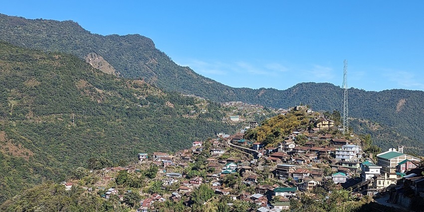 A scenic view of a village in Nagaland, India, showcasing terraced fields, traditional Naga huts, and lush green hills