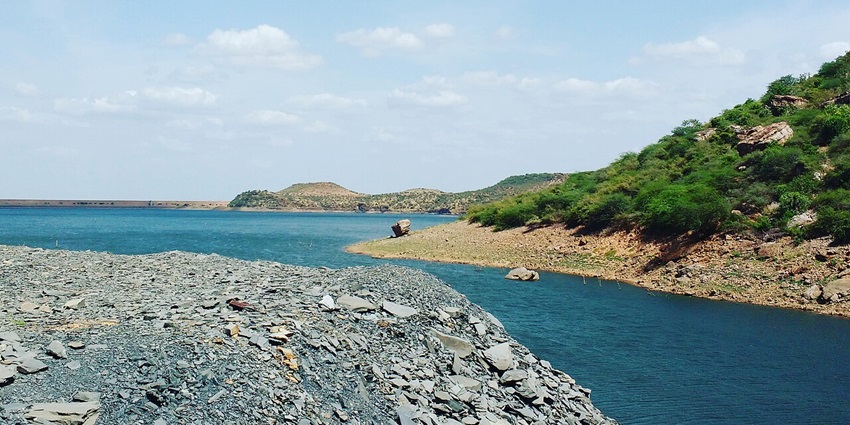 Tranquil OWK Reservoir nestled between lush hills under blue skies, reflecting serene waters in Andhra Pradesh.