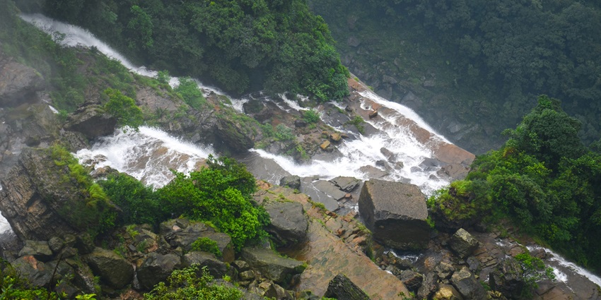 A scenic view of water gushing through the giant rocks and lush greenery in the region.
