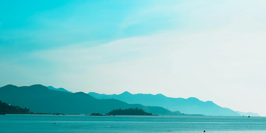 A picture of a beautiful landscape with a beach and ocean in front of a mountain range