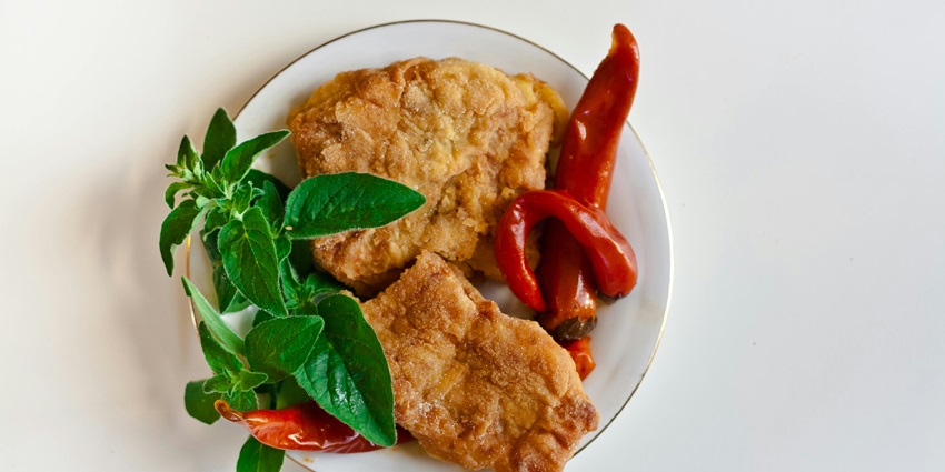A mouth-watering view of a white plate served with fried chicken garnished with greens.