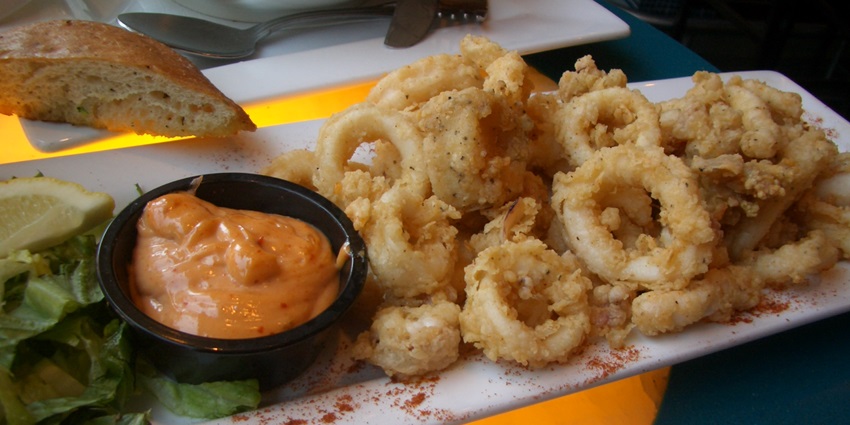 Plate of Fried squid rings served with a spicy sauce alongside.