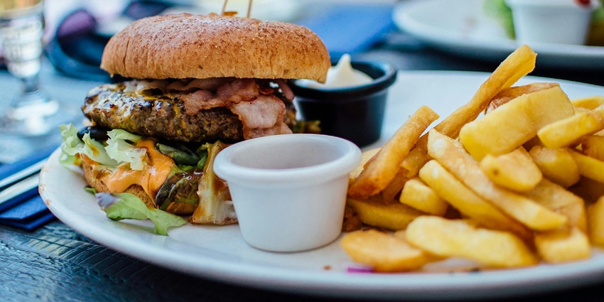 Fries and burger served on a plate, with the burger stacked high and fries on the side.