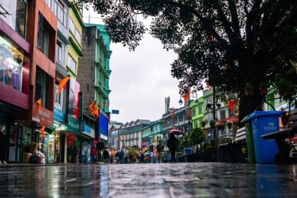 A breathtaking view of a market in Gangtok with wet roads and people walking down it.