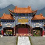 An outer scenic view of the monastery with verdant hills and a collected mist of clouds.