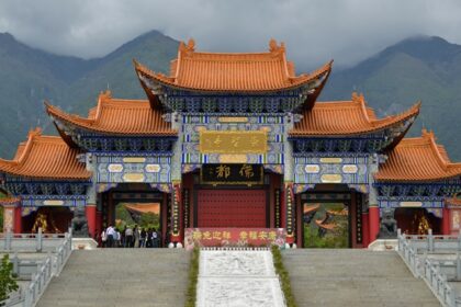 An outer scenic view of the monastery with verdant hills and a collected mist of clouds.