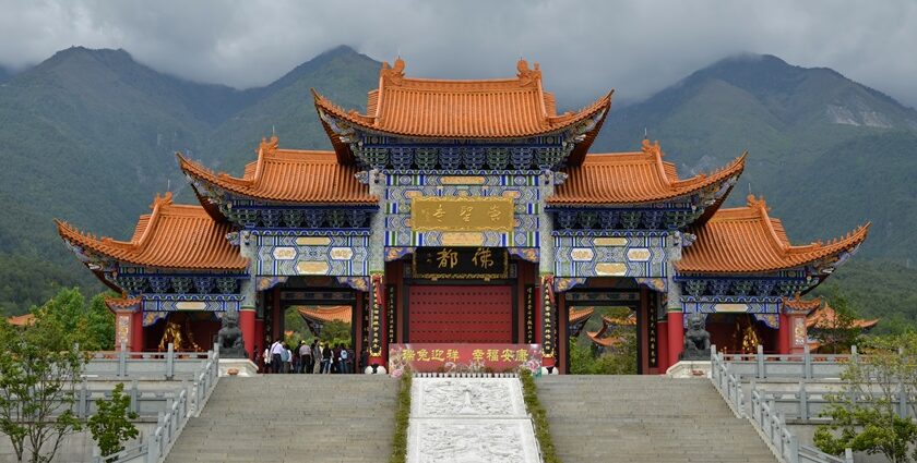 An outer scenic view of the monastery with verdant hills and a collected mist of clouds.